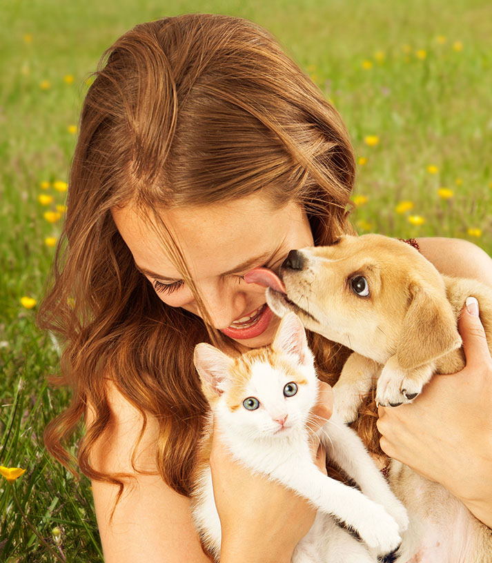 woman getting kisses from puppy while also holding kitten